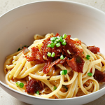 Kimchi Carbonara: Creamy carbonara pasta with spicy kimchi, bacon bits, and a sprinkle of sesame seeds. The dish is served in a white bowl and garnished with green onions.