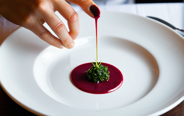 A close-up, top-down view of a sophisticated fusion cuisine dish, presented as a work of art on a minimalist white ceramic plate. The dish features vibrant, contrasting colors from fresh ingredients like red beet puree, green herb oil, and delicate white seafood, with varied textures including a crisp element and a smooth, creamy sauce. Artistic sauce drizzles enhance the visual appeal. The setting is a brightly lit, professional fine dining restaurant table, with soft, diffused light highlighting the food. Fully clothed, appropriate content, safe for work, professional, perfect anatomy, correct proportions, natural pose, well-formed hands, proper finger count, high-resolution, sharp focus, gastronomic photography, studio lighting.